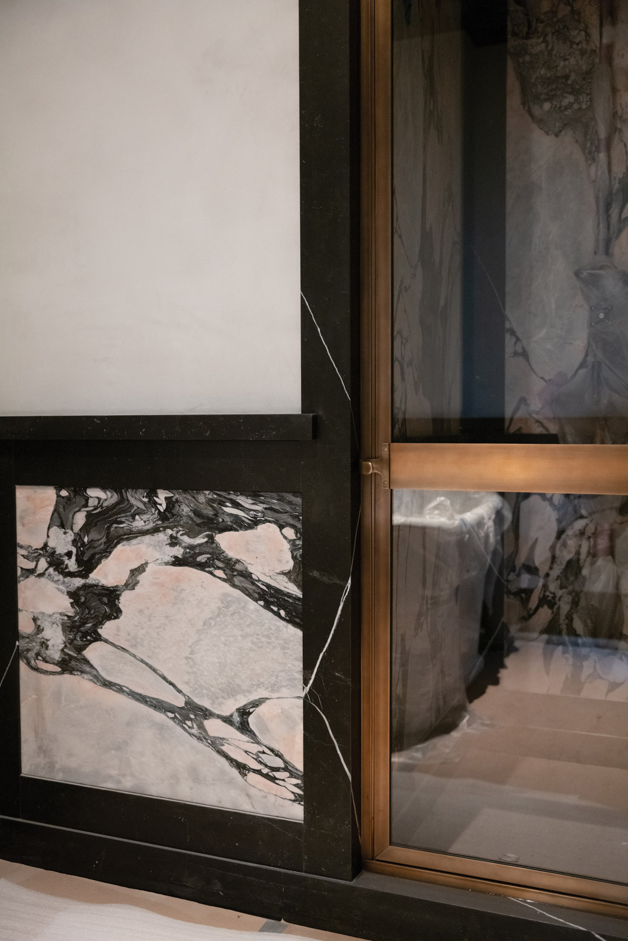 A bronze-framed shower door matches the elegance of Black Venato marble framing the doorway in a guest bathroom.