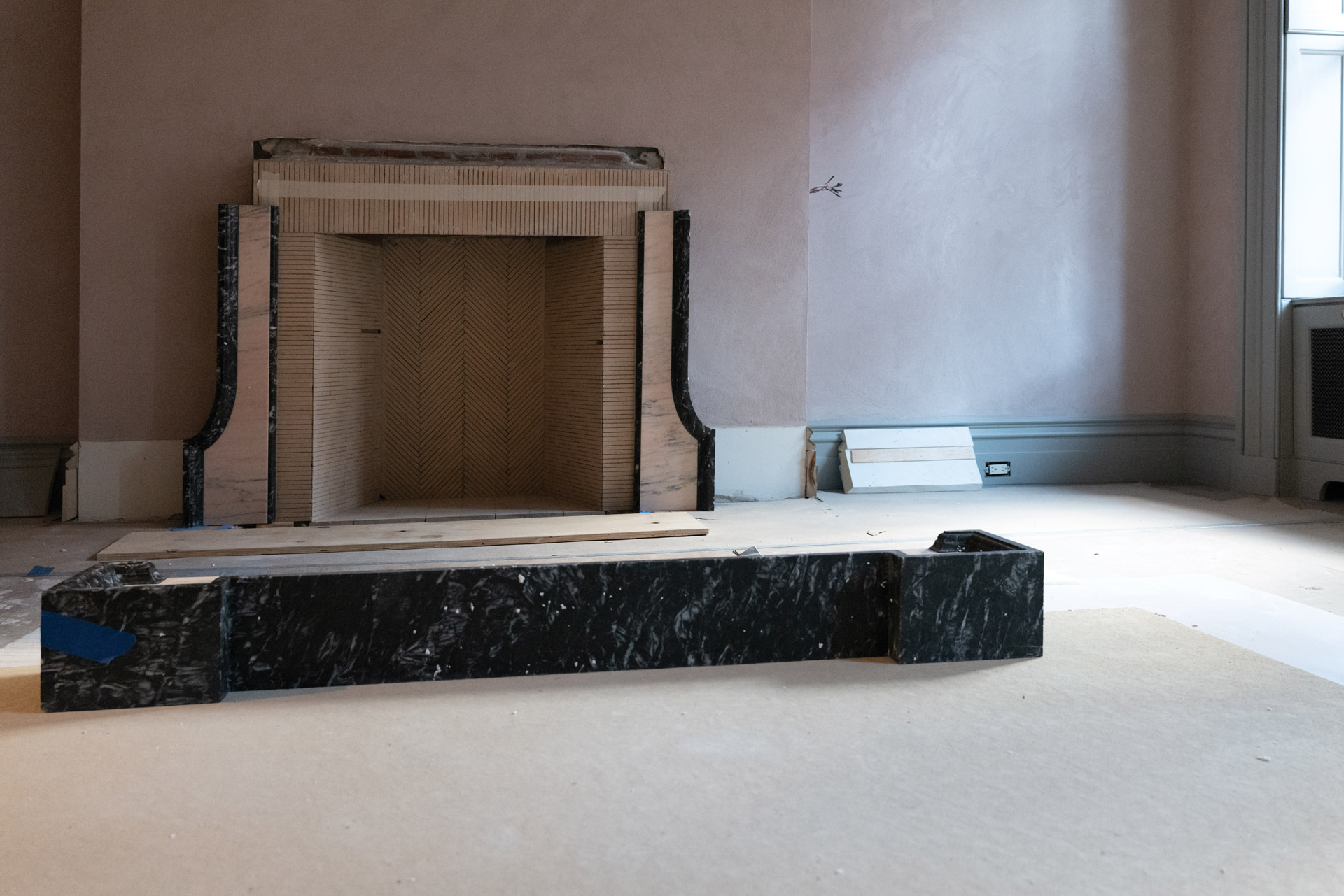 The final piece of a Black Levandia frame awaits installation atop a guest room fireplace faced in Portugal Pink Borba.